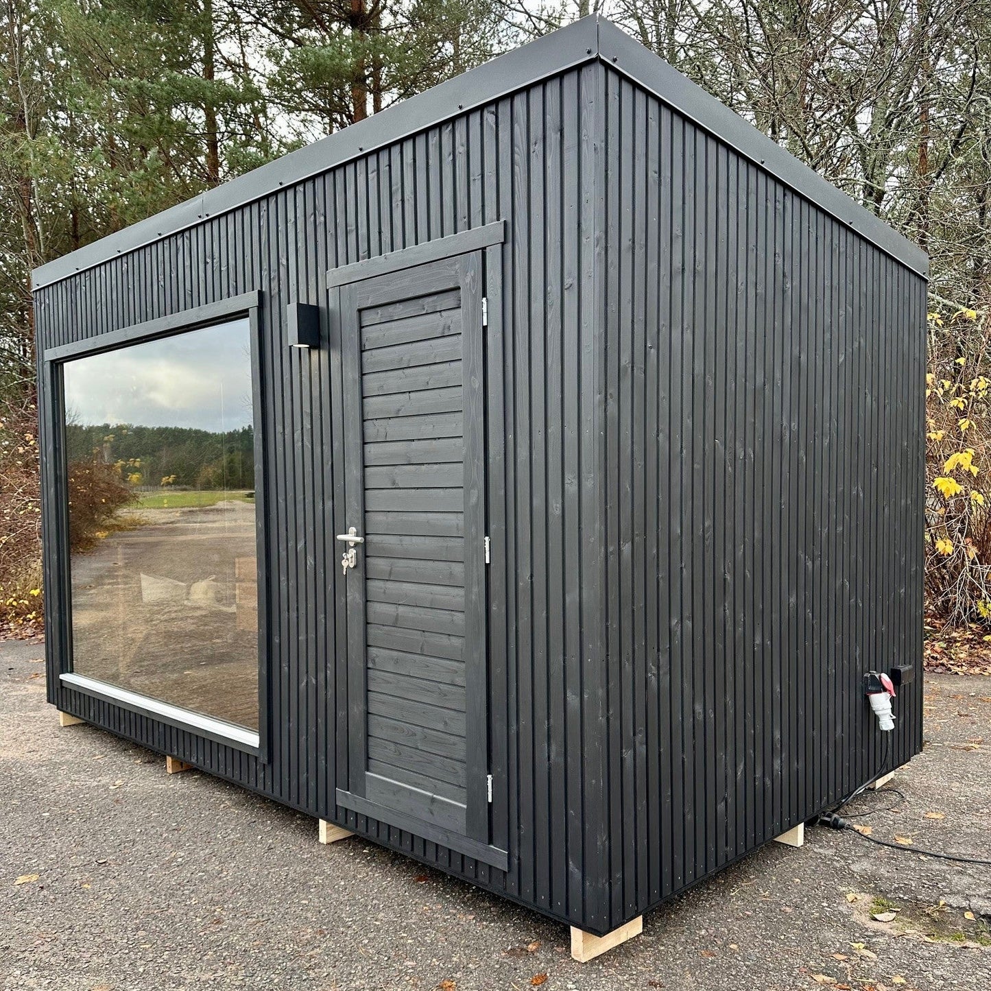 Modern blackprefab building with a door and window in a natural setting.
