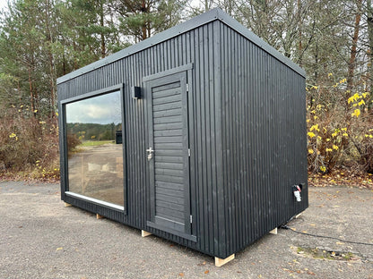 Black modular building with glass door and window in a forest setting