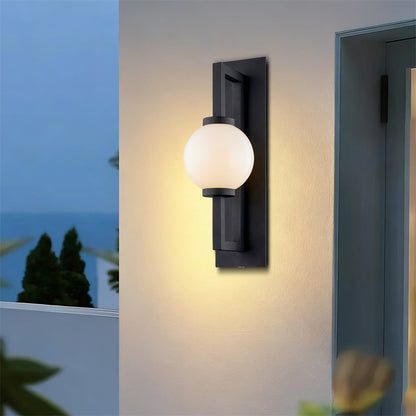 Orb outdoor wall light glowing warm white on rendered garden wall at dusk