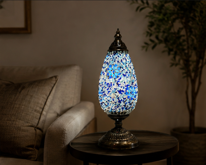 Serena mosaic table lamp glowing with blue, white and turquoise glass on a side table beside a sofa in a dimly lit living room