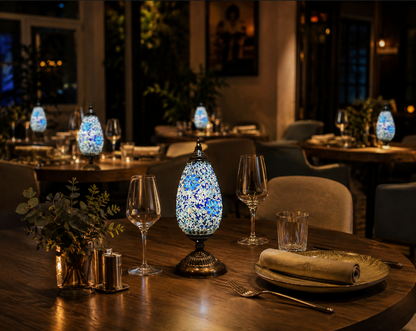 Blue and white mosaic table lamp glowing on a restaurant dining table with wine glasses and a napkin